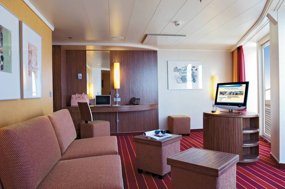 Deluxe-Suite der AIDAbella mit großem Wohnbereich, Sofa, Schreibtisch und Flachbildschirm.