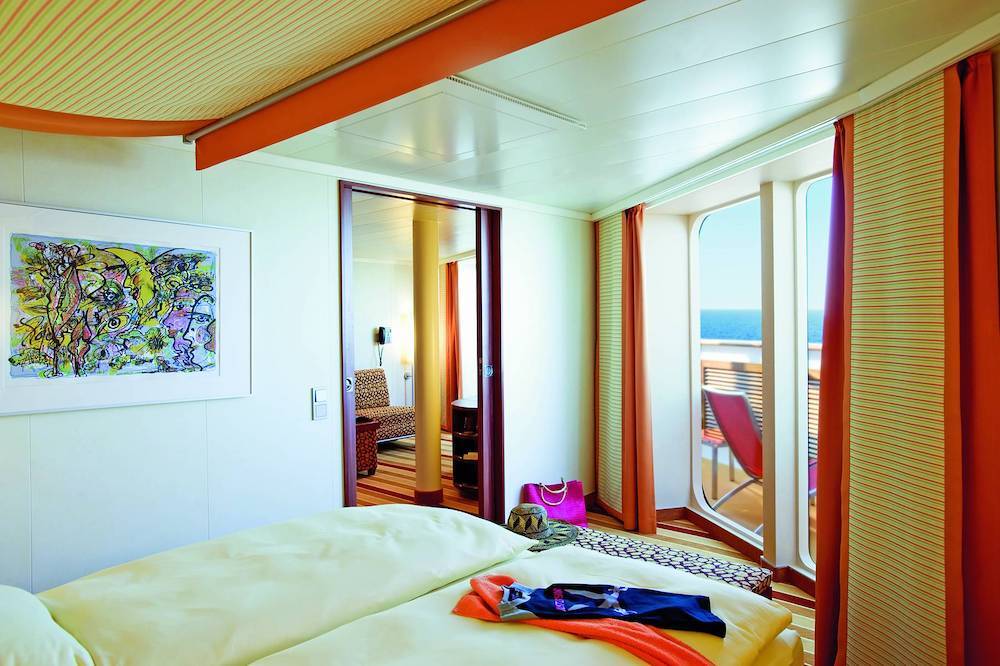 Premium-Suite auf der AIDAbella mit Doppelbett, Wohnbereich, Balkon und Blick auf das Meer