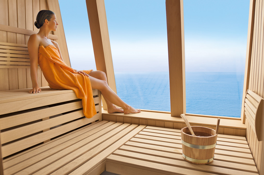 Frau in Sauna mit Holzsitzbänken und Meerblick durch das Fenster