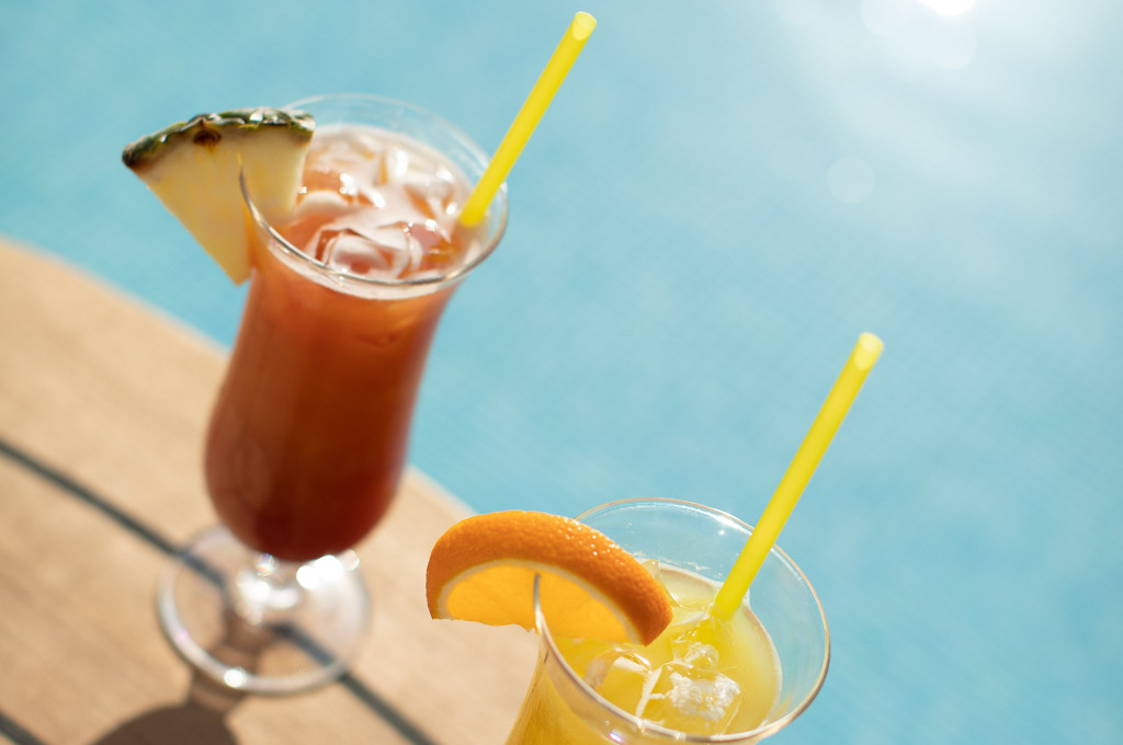 Bunte Cocktails auf dem Sonnendeck mit türkisblauem Wasser und gelbem Trinkhalm.