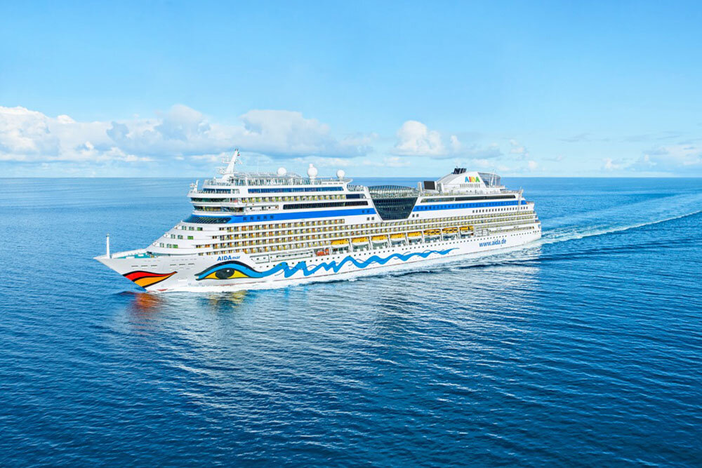 Kreuzfahrtschiff mit Kussmund am Bug und mehreren Balkondecks fährt bei Sonnenschein auf tiefblauem Meer