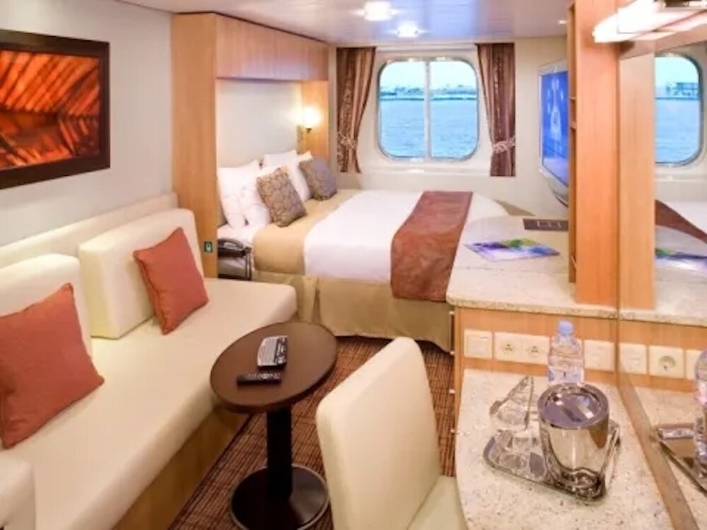 Außenkabine mit Doppelbett, Bullauge und Sofa auf einem Hochseekreuzfahrtschiff