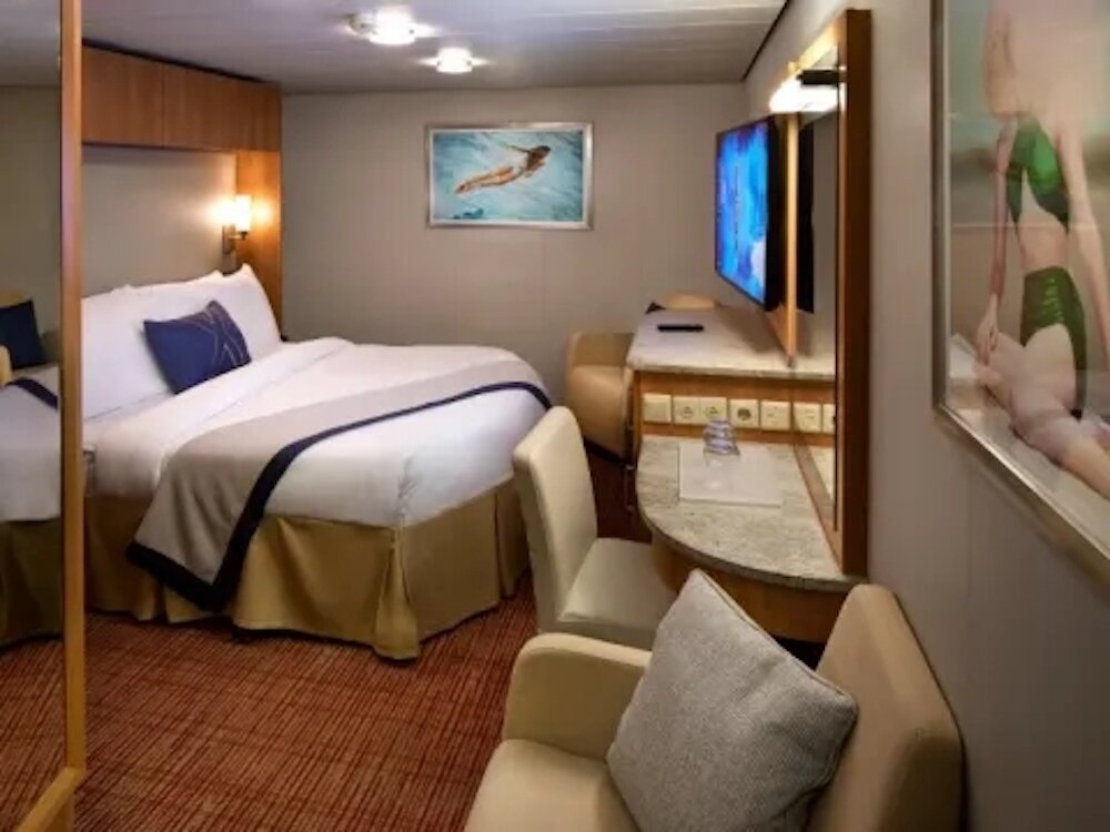 Innenkabine mit Doppelbett, Sesseln und Flatscreen-TV auf der Celebrity Reflection