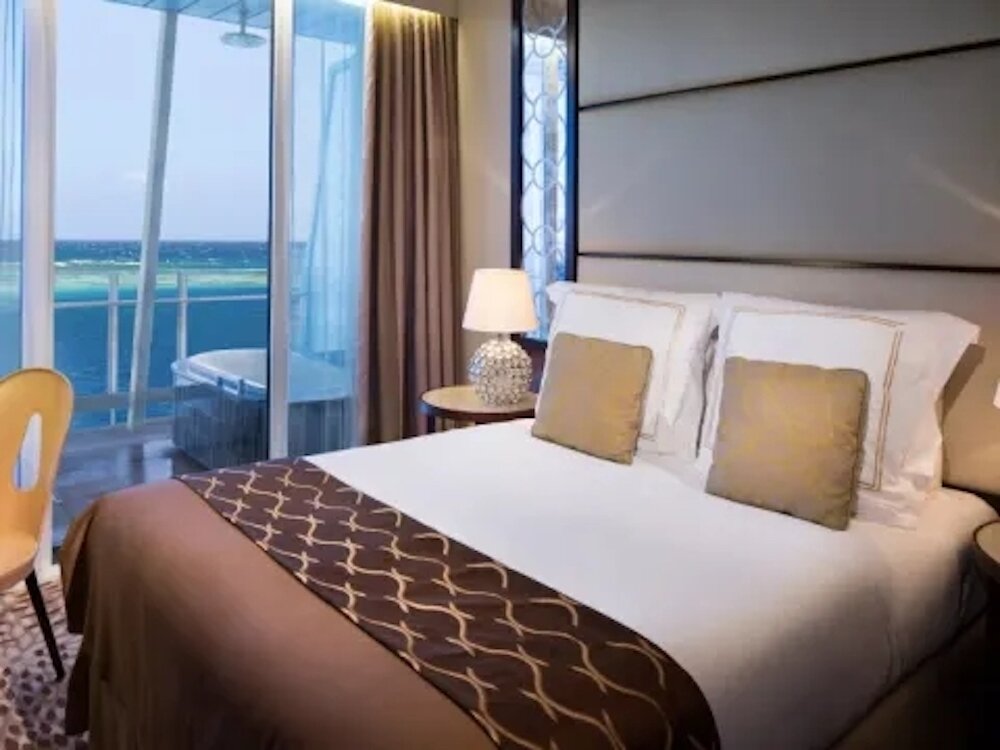 Penthouse Suite der Celebrity Reflection mit Doppelbett und großzügigem Balkon mit Außenbadewanne und Meeresblick.