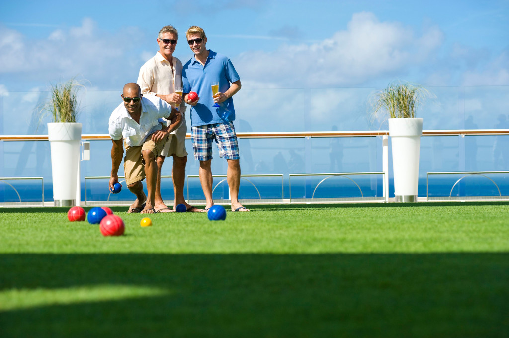 Gäste spielen Bowlingkugel-Spiel auf dem rasenartigen Außendeck mit Meerblick.