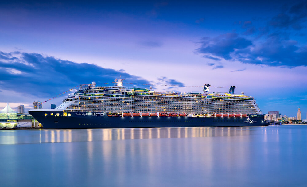 Celebrity Reflection fährt durch ruhige Gewässer mit Hafenkulisse im Hintergrund