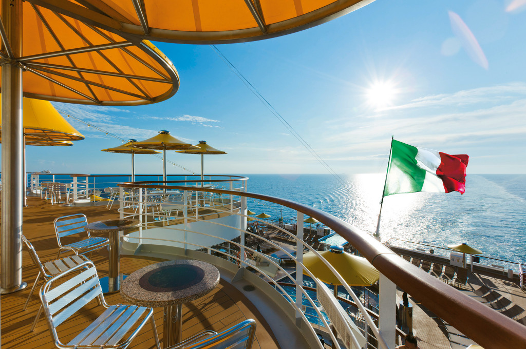 Costa Fascinosa Sonnendeck mit Liegestühlen, Sonnenschirmen, italienischer Fahne und Meerblick.