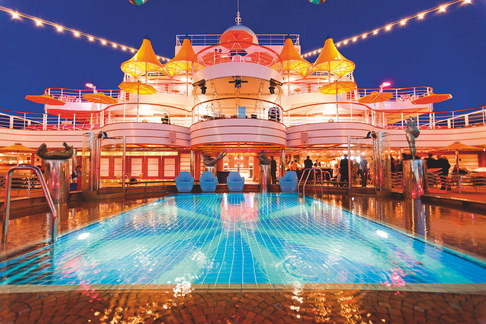 Beleuchteter Pooldeck der Costa Fascinosa bei Nacht mit Pool, Sonnenschirmen und mehreren Decksebenen