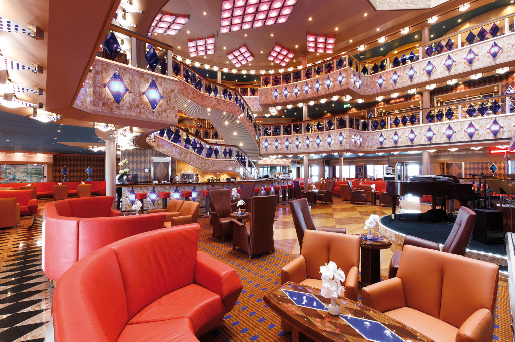 Costa Favolosa Atrium mit mehreren Etagen, roten Loungesofas und eleganter Innenarchitektur.