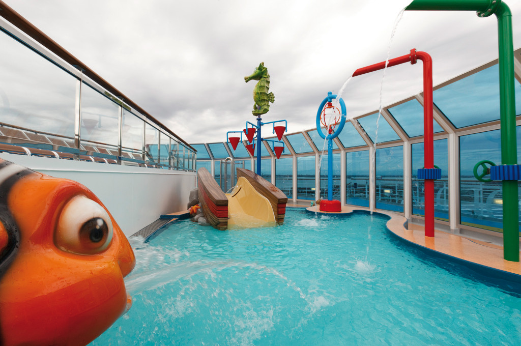 Costa Favolosa Kinderpool mit farbigen Wasserspielgeräten und Meerwasser-Panoramafenstern.