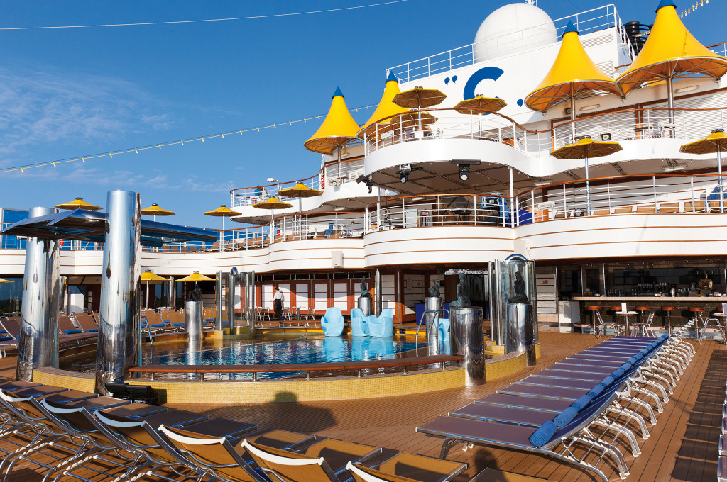 Costa Favolosa Poolbereich mit Sonnenschirmen, Liegestühlen und Schiffsoberbau im Sonnenlicht.