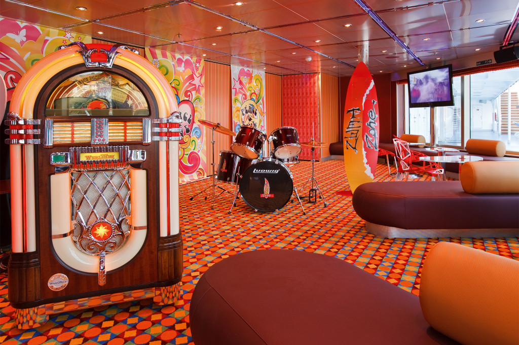 Teen Zone mit Jukebox, Schlagzeug, buntem Design und farbigen Sitzmöbeln für junge Passagiere.
