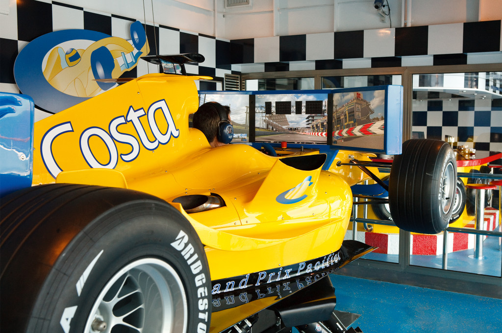 Formel 1-Simulator mit gelbem Rennwagen, Bildschirmen und kariertem Bodenbelag für Motorsport-Enthusiasten.