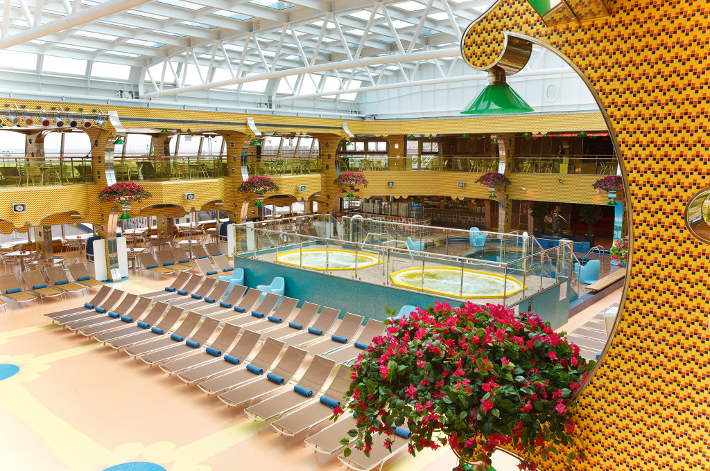 Lido Deck mit großem indoorpool, Liegestühlen und gelbem Sichtschutzdach an Bord der Costa Pacifica.