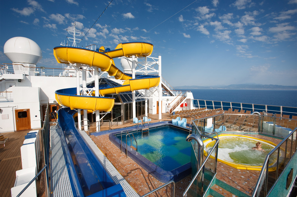 Pooldeck mit gelber Wasserrutsche, Pools und Liegebereich mit Meerblick auf der Costa Pacifica.