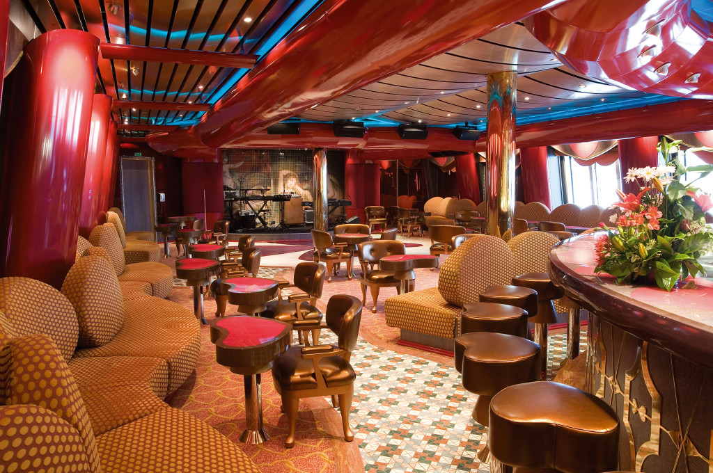 Bar mit roter Innenausstattung, braunen Sesseln, roten Hocker-Tischen und dekorativen Holzpilastern.
