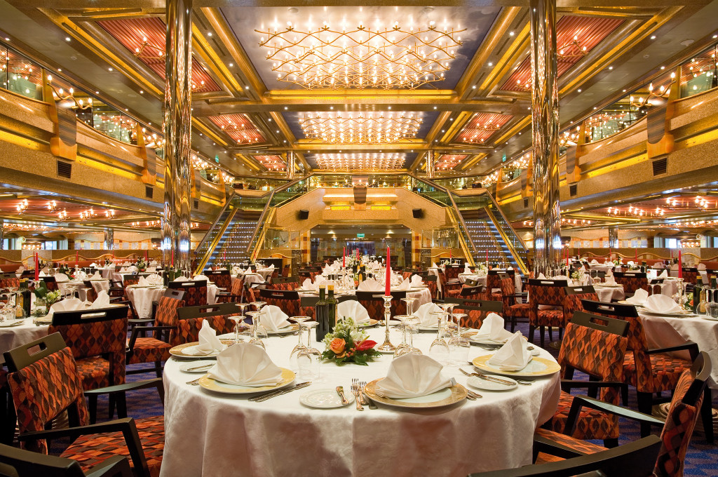 Großer Speisesaal mit goldenen Leuchten, mehreren Ebenen und eleganten Tischen mit Meerblick.