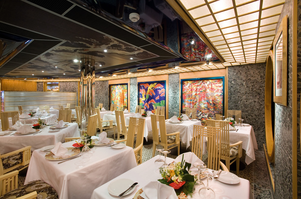 Restaurant mit modernem Design, farbigen Kunstwerken, eleganten Holzstühlen und weißen Tischtüchern.