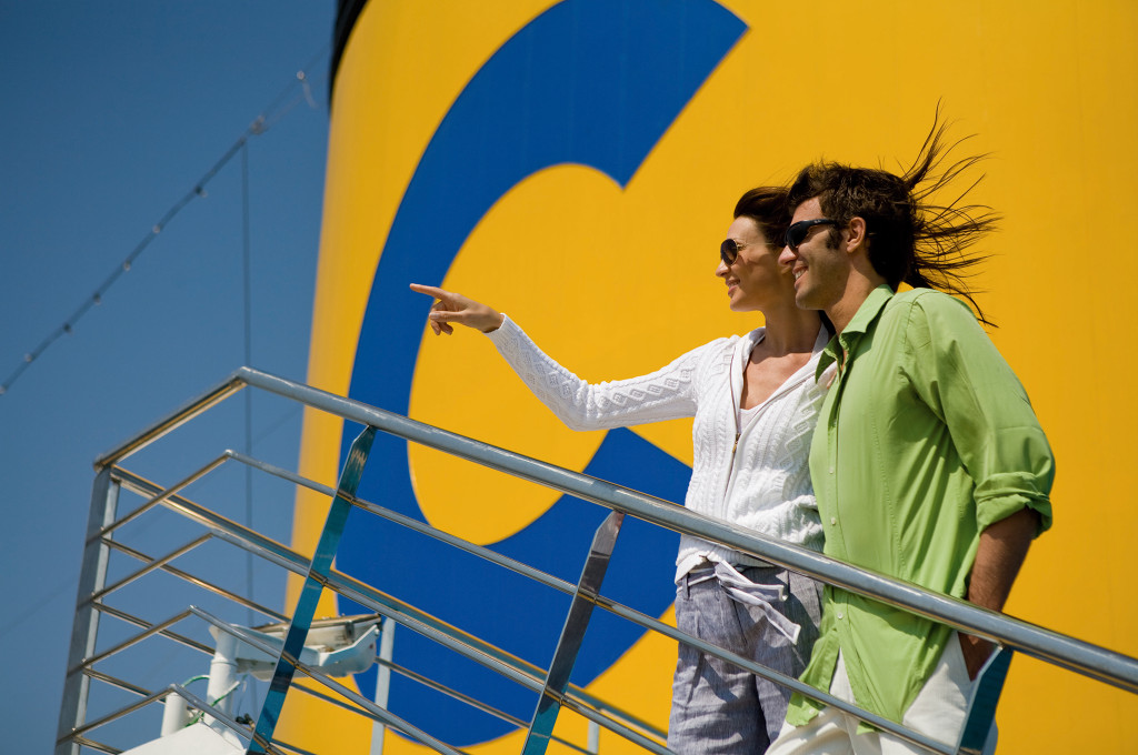 Passagiere auf dem Außendeck eines Kreuzfahrtschiffs mit Blick aufs Meer