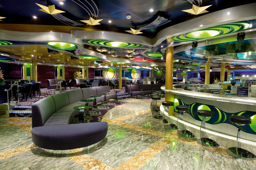 Luna Lounge mit grüner und gelber Dekoration, modernen Leuchten und geschwungenen Sitzmöbeln.