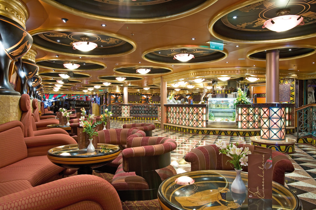 Luna Lounge mit roten Sesseln, Golddekorationen und eleganten Tischen für Entspannung an Bord.