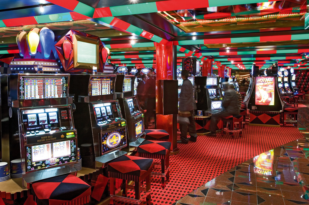 Casino mit roten und grünen Elementen, vielen Spielautomaten und bunter Deckenbeleuchtung an Bord.