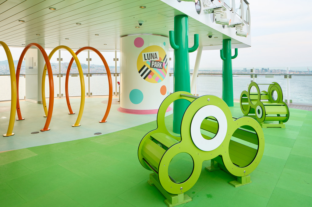 Kinderspielbereich Luna Park auf dem Außendeck der Costa Smeralda mit bunten Spielgeräten und Hafen im Hintergrund.