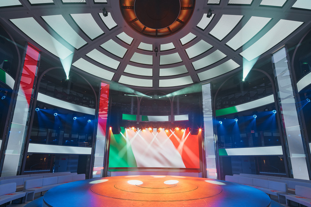 Atrium Colosseo auf der Costa Smeralda mit Rundkuppel, bunter Lichtshow und beleuchteter Bühne.