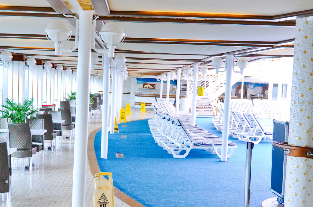 Überdachter Poolbereich mit weißen Liegestühlen und Sitzplätzen auf dem Außendeck der Grand Princess.