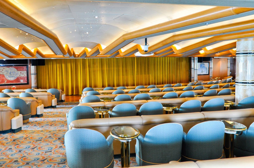 The Lodge Lounge mit modernen blauen Sesseln, goldenen Leuchten und eleganter Architektur auf der Grand Princess.