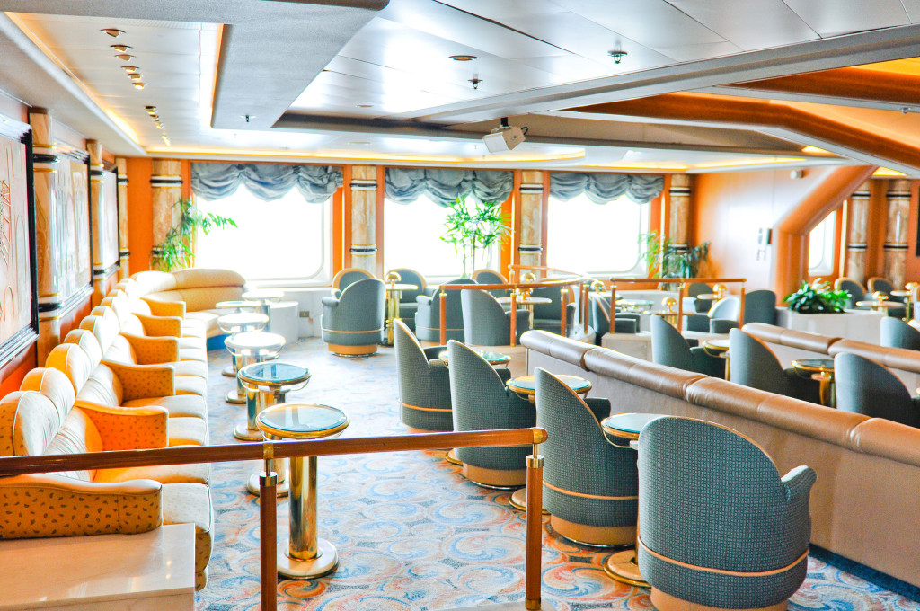 Elegante Lounge mit orangenen Wandelementen, grünen Pflanzen und stilvollen Sitzecken auf der Grand Princess.