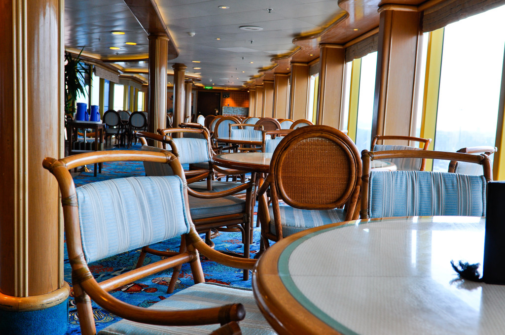 Elegante Lounge mit Rattan-Sesseln, Sitzbereichen und Fensterblick auf der Grand Princess.