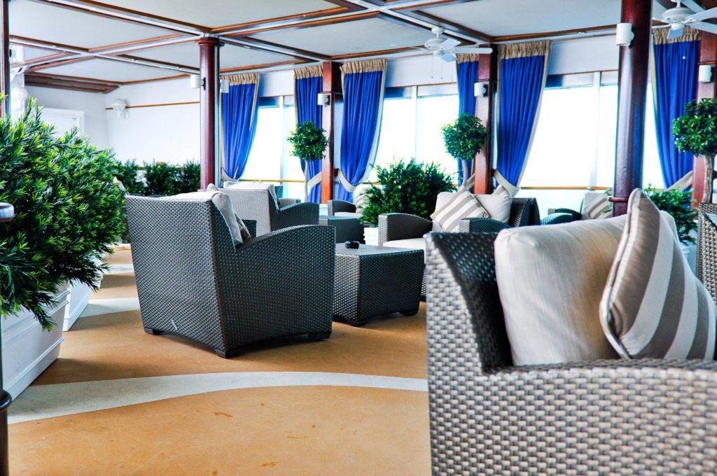 Moderne Lounge mit gepolsterten Möbeln, grünen Pflanzen und Fensterdekor auf der Grand Princess.