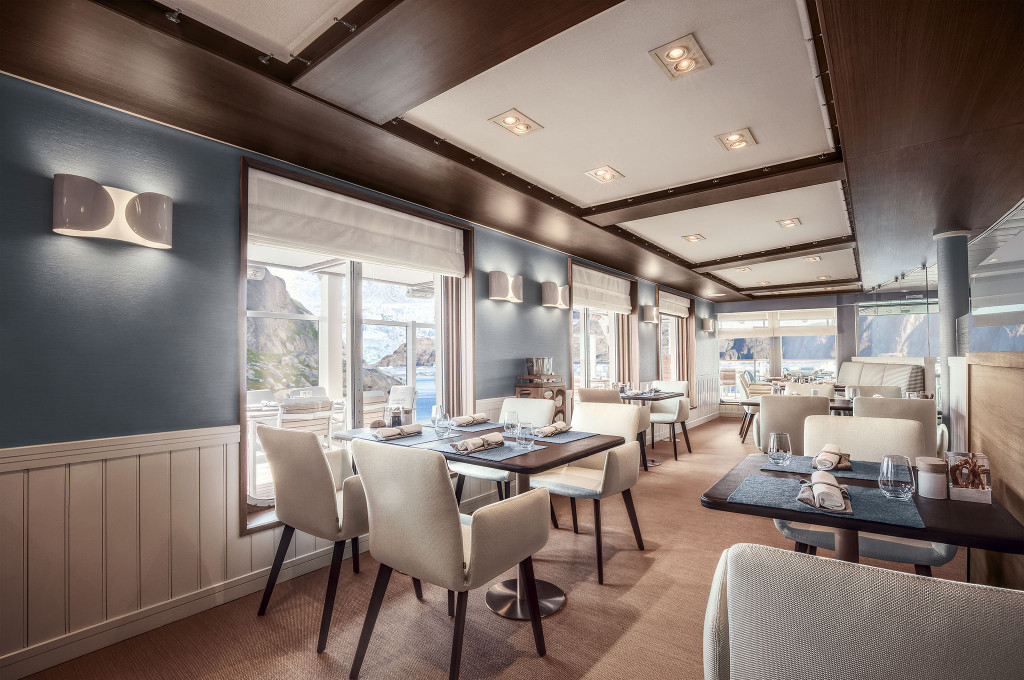 Lido-Restaurant mit cremefarbenen Stühlen, gedeckten Tischen und Blick durch Panoramafenster auf arktische Felsenküste