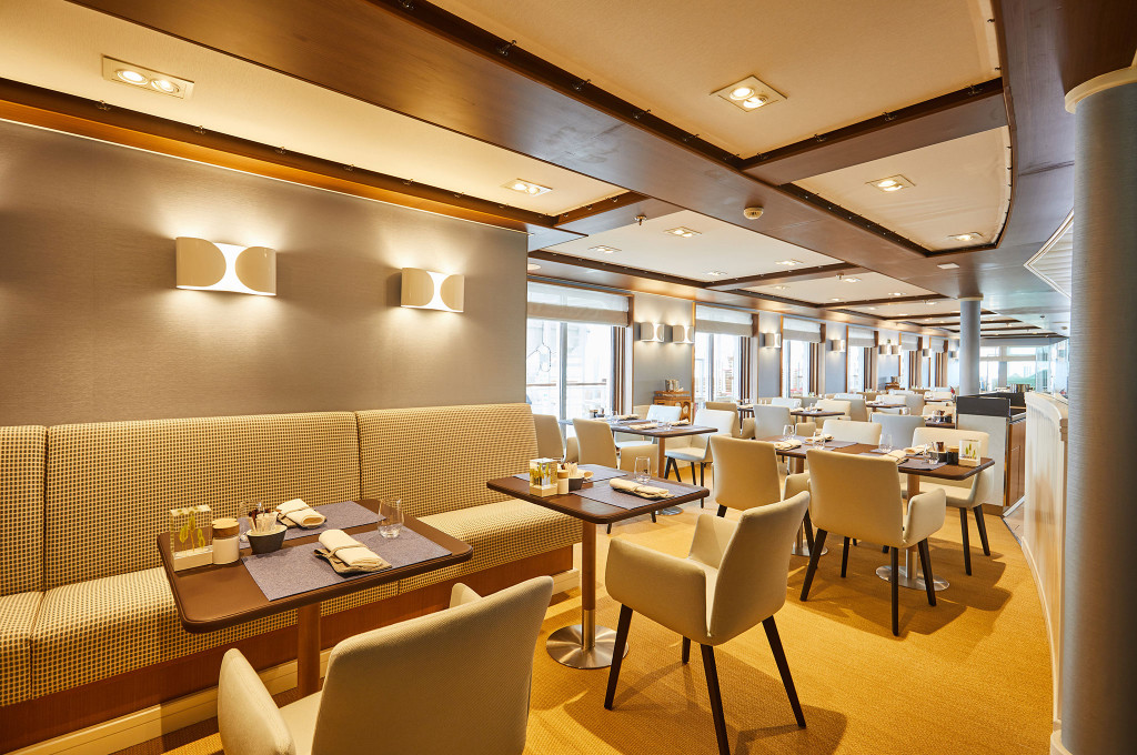 Helles Lido-Restaurant mit gemusterten Sitzbänken, gedeckten Tischen und Panoramafenstern auf einem Expeditionskreuzfahrtschiff