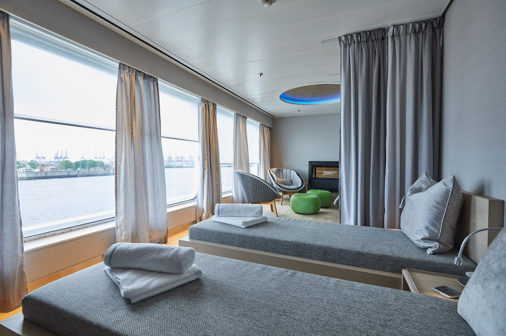 Spa-Ruhebereich mit Liegebetten, Sesseln, kleinem Kamin und Panoramafenstern mit Hafenblick