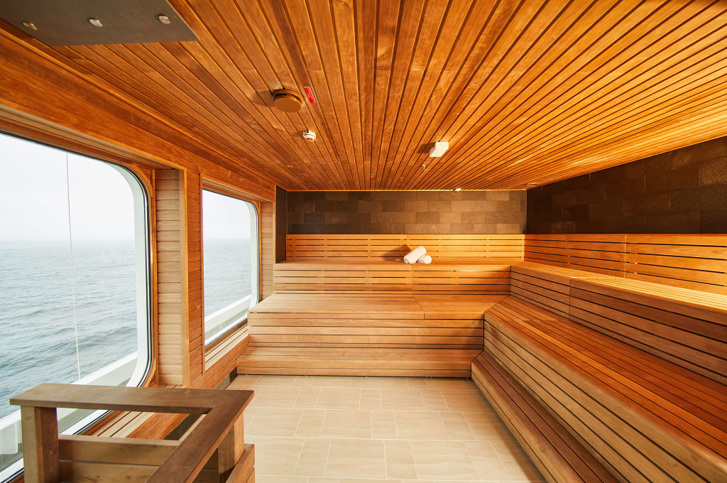 Holzsauna mit Schieferwand, mehrstufigen Holzbänken, Handtüchern und Panoramafenster mit Meerblick