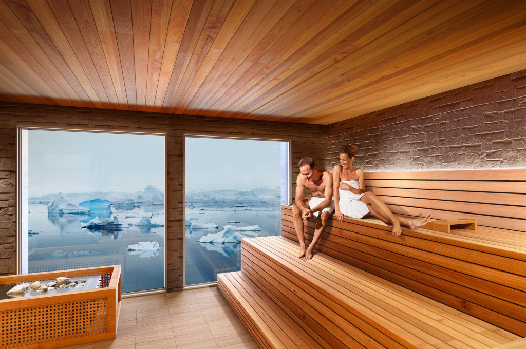 Holzsauna mit großen Panoramafenstern und Blick auf treibende Eisberge in arktischem Gewässer