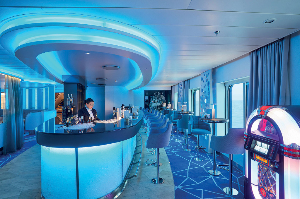 Bar mit leuchtend blauem Ringdecken-Design, geschwungener Theke, Barstuhlreihe, Jukebox und Panoramafenster mit Meerblick