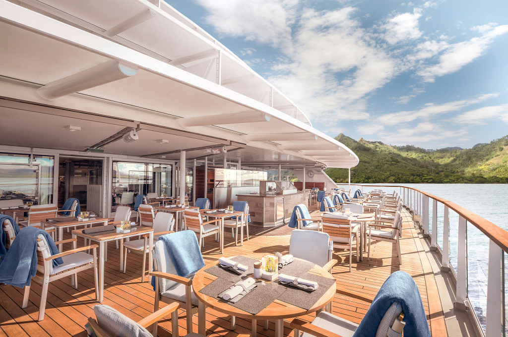 Außenterrasse des Lido-Restaurants mit Teakdeck, gedeckten Holztischen und Blick auf tropisch-grüne Hügellandschaft