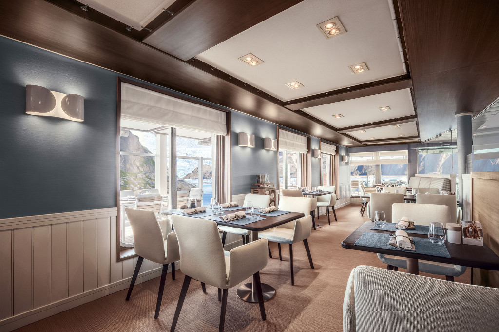 Lido-Restaurant mit cremefarbenen Stühlen, gedeckten Tischen und Blick auf arktische Felsenküste durch Panoramafenster