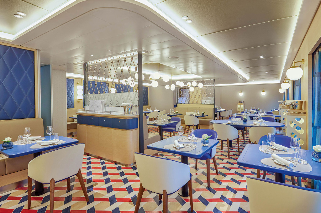 Spezialitätenrestaurant mit geometrischem Teppich, blauen Tischen, cremefarbenen Stühlen und Kugelleuchten-Clustern