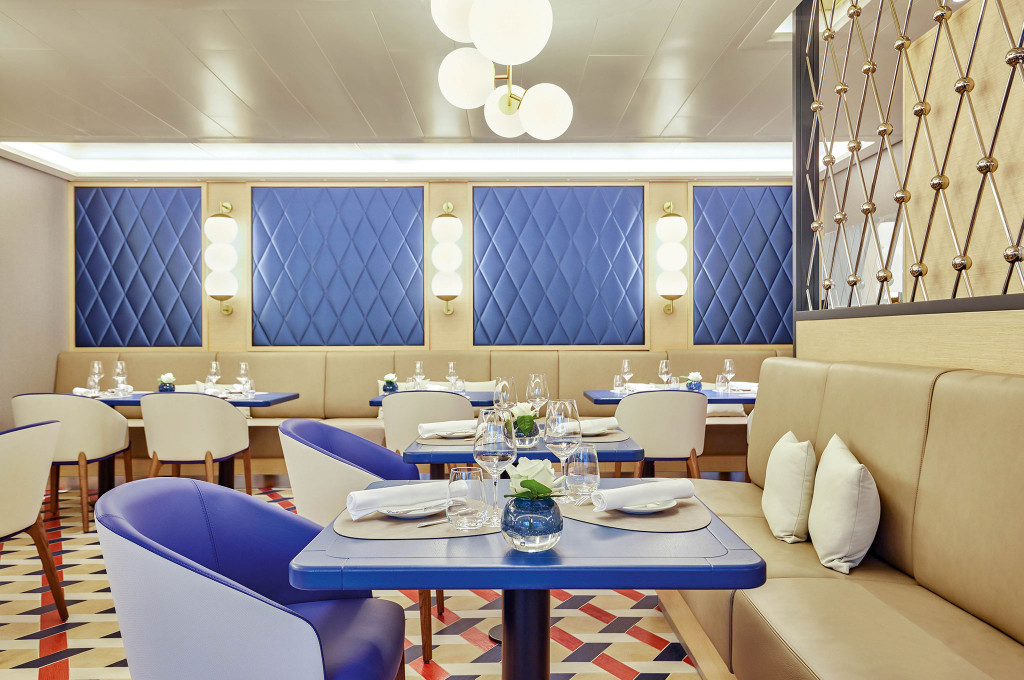 Spezialitätenrestaurant mit blauen Ledersesseln, cremefarbener Sitzbank, blau gesteppten Wandpaneelen und Kugelpendelleuchten