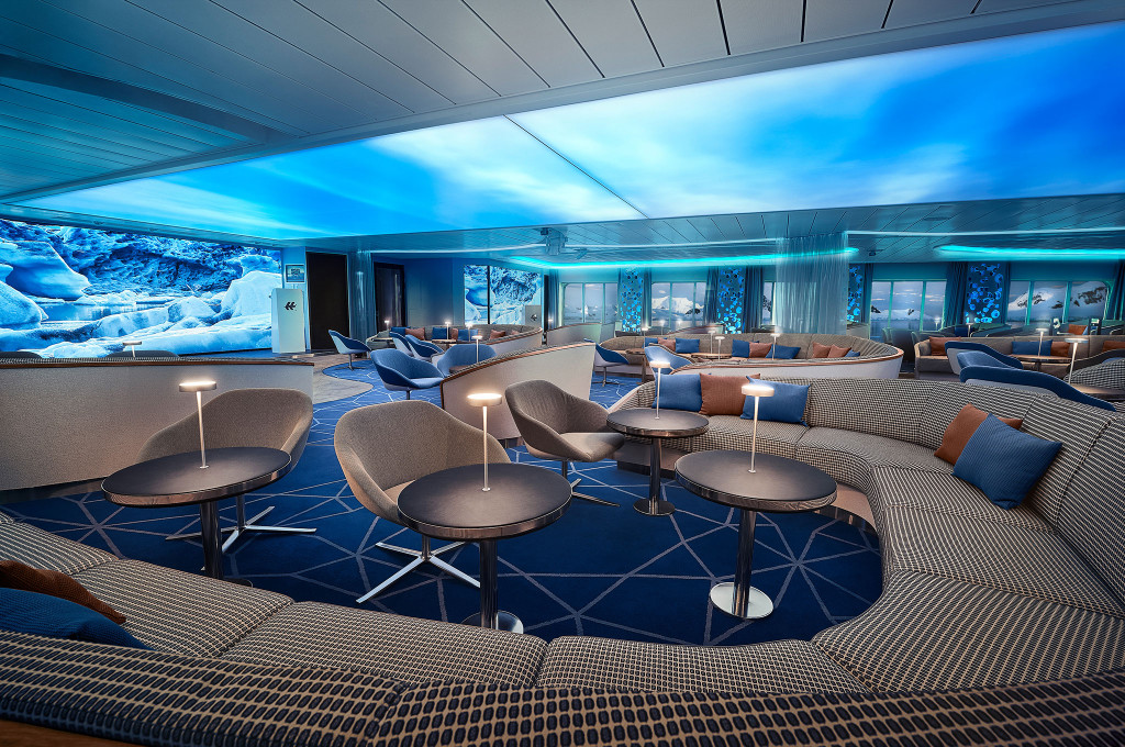 HanseAtrium-Lounge mit beleuchtetem Deckenpaneel, gemusterten Rundsofas, Tischlampen und LED-Panoramawand mit arktischem Gletschermotiv