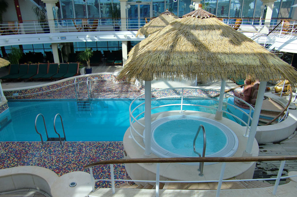 Poolbereich mit Whirlpool unter Sonnenschirm und Liegen auf der Island Princess.