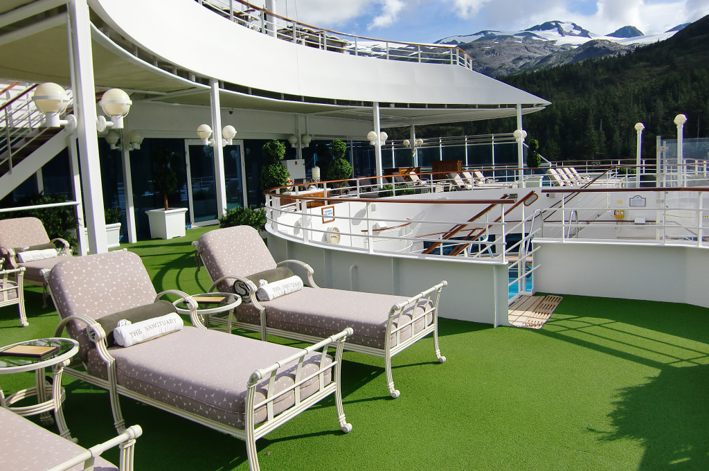 The Sanctuary Ruhebereich mit gepolsterten Liegen auf dem Sonnendeck der Island Princess mit Blick auf schneebedeckte Berge in Alaska.