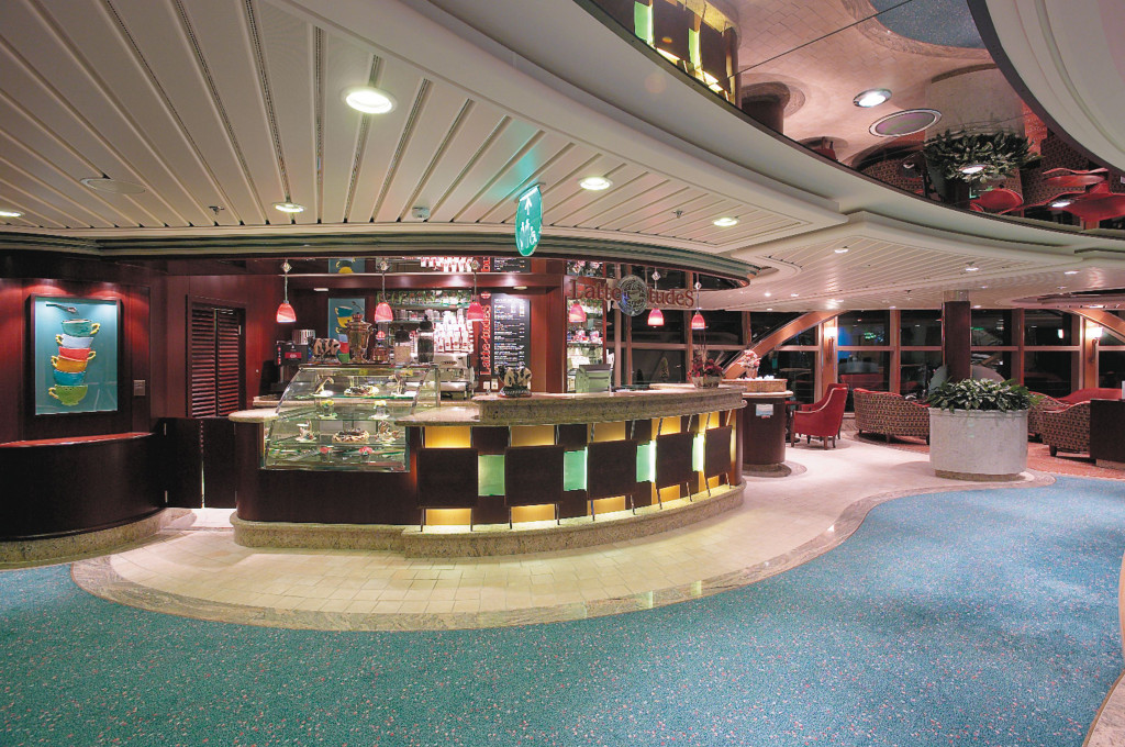 Kaffeebar Latte-tudes mit beleuchteter Kuchenvitrine und Sitzgelegenheiten im Promenadenbereich des Schiffes.