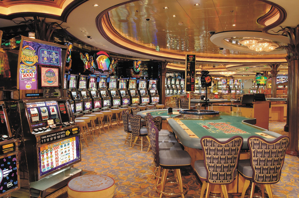 Bordcasino mit Reihen von Spielautomaten, Roulette-Tischen und Barhockern unter dekorativer Deckenbeleuchtung.