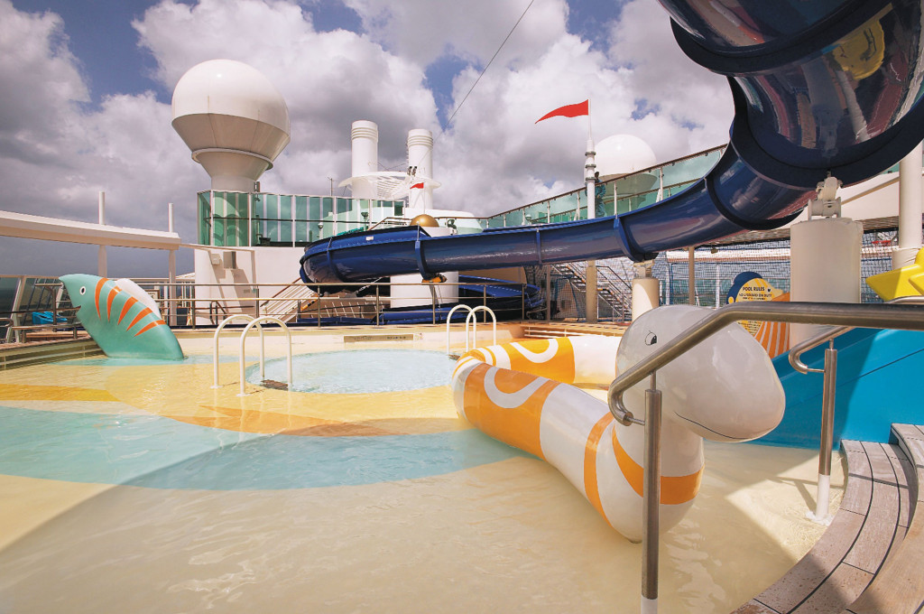 Planschbecken mit blauer Wasserrutsche, bunten Spielfiguren und flachem Kinderpool auf dem Außendeck des Schiffes.