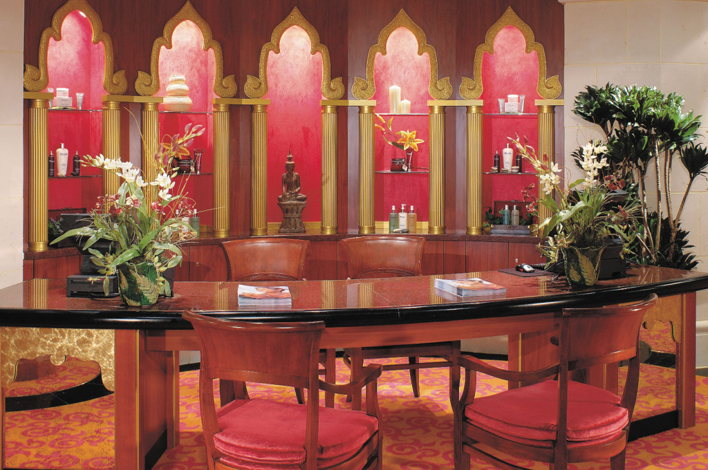 Spa-Rezeption mit Buddha-Figur, goldenen Säulen und Pflegeprodukten in orientalisch-asiatischer Gestaltung.